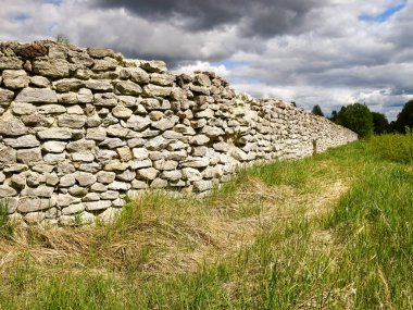 Beyaz bir dağın ve yeşil ağaçların üzerinden geçen taş bir çitin ötesine bak.