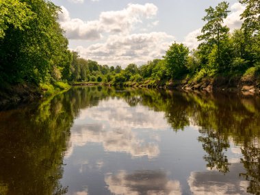 Nehirli yaz manzarası, kıyılarda yeşil ağaçlar ve bulutlar, güzel bir parıltı.