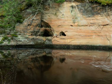 Dik bir nehri olan ve kumtaşı kayalıklarda mağaraları olan bir manzara.
