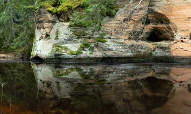 Dik bir nehri olan ve kumtaşı kayalıklarda mağaraları olan bir manzara.