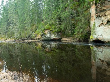 Dik bir nehri olan ve kumtaşı kayalıklarda mağaraları olan bir manzara.