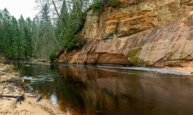 Dik bir nehri olan ve kumtaşı kayalıklarda mağaraları olan bir manzara.