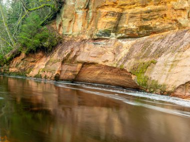 Dik bir nehri olan ve kumtaşı kayalıklarda mağaraları olan bir manzara.
