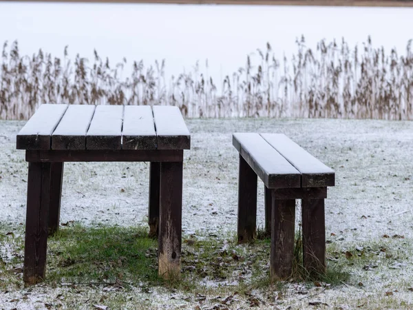 Landscape with a snow-covered wooden table and a bench by the la — Stock Photo, Image