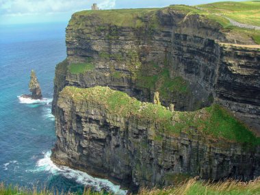 Renkli okyanus manzarası, yeşil çimenli kayalar, kayalar ve mavi su. İrlanda 'daki Moher Kayalıkları