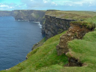 Renkli okyanus manzarası, yeşil çimenli kayalar, kayalar ve mavi su. İrlanda 'daki Moher Kayalıkları
