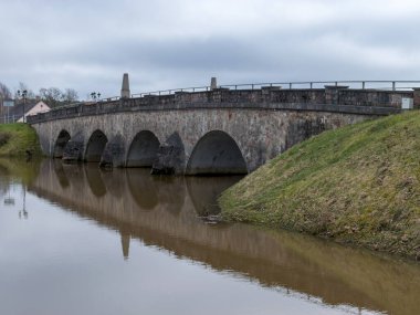 İlkbaharda taşan nehir manzarası, nehir üzerinde kemerli taş köprü, suda ayna yansıması.