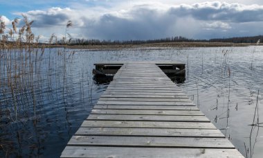 Merkezinde tahta yaya köprüsü, göl ve gökyüzü arkaplanı olan manzara