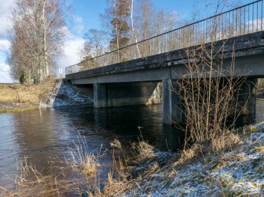 Köprüsü olan bahar manzarası, ön planda eski çimlerin ve çalıların resimleri.