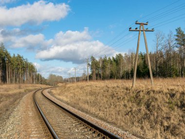 Tren rayları, ilkbahar başları, kuru çimenler, güzel mavi gökyüzü ve beyaz bulutlar.
