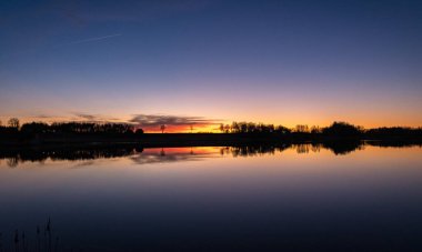 Göl kenarında güzel bir gün batımı, parlak renkler, göl suyunda gökyüzü yansımaları.