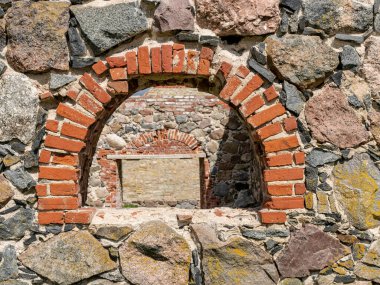 Eski bir taş bina duvarı ve kavisli pencereleri olan bahar manzarası. Parlak yeşil bir arazideki bir binanın kalıntıları.
