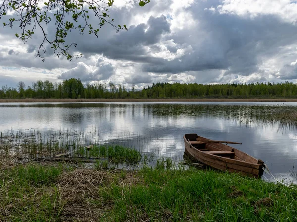 gorgeous spring landscape with calm lake water, wonderful cloud reflections in the lake water, a beautiful brown wooden boat on the lake shore