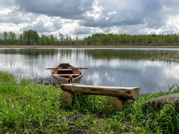 beautiful landscape with calm lake water, white cumulus clouds and reflections in the water, brown wooden boat on the lake shore, wooden bench in the foreground