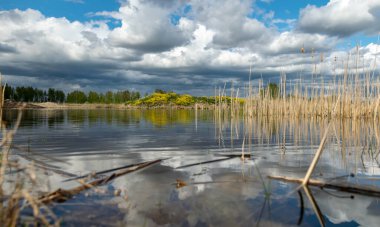 Kümülüs bulutlarının gölde yansıdığı güzel, sakin bir gökyüzü manzarası. Geçen yılın kuru sazları.