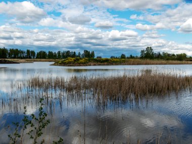 Kümülüs bulutlarının gölde yansıdığı güzel, sakin bir gökyüzü manzarası.