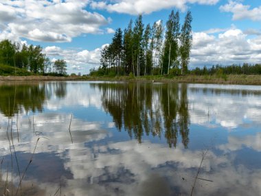 Kümülüs bulutlarının gölde yansıdığı güzel, sakin bir gökyüzü manzarası.
