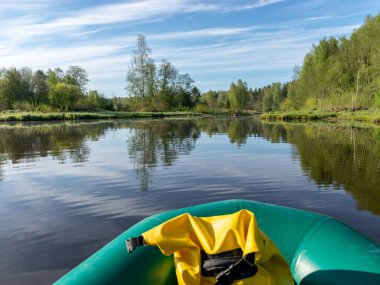 Yeşil bir balıkçının lastik teknesinden nehir manzarası, yansımalı sakin nehir suyu ve kıyıdaki parlak yeşil bitki örtüsü.