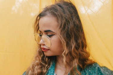 Arka planda sarı bez üzerine gözlük takan genç hippi modern kadın. Kıvırcık kahverengi saçlı.