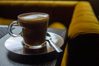 Sıcak ve hoş kafeteryada hardal renkli kanepenin yanında bir fincan kahve..