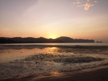 Arkasında dağlar olan kumlu bir sahilde egzotik bir gün doğumu..