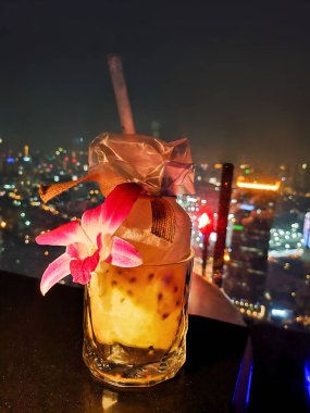 Büyük şehirdeki gökdelenin çatısındaki bir barda pahalı bir alkollü tutku meyvesi içeceği. Bangkok, Tayland 'da şehir ışıklarının gece görüşü olan bir gökyüzü barı