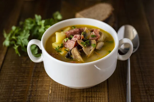 Hot soup with meat and mushrooms in a white plate on a beautiful wooden background
