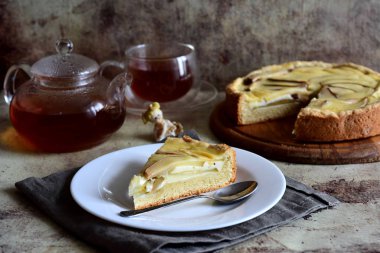 Ahşap bir tabakta lezzetli armut turtası, bir fincan sıcak çay, gri arkaplanda çay olan çaydanlık.