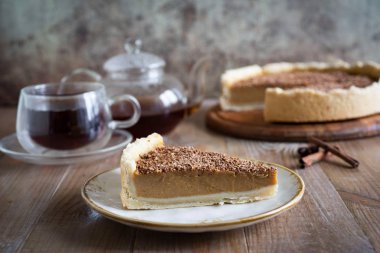 Bir parça balkabağı turtası, antika bir tabakta, yakın plan. Arka planda, bir balkabağı turtası ve bir fincan sıcak çay..