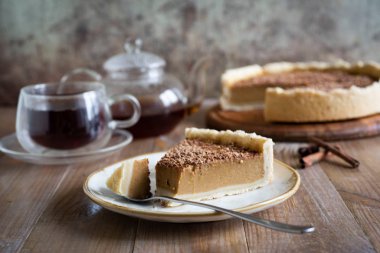 Eski bir tabakta, bir parça balkabağı turtası ve bir kaşık. Arka planda lezzetli bir kabak turtası, çikolatalı ve bir fincan çay.