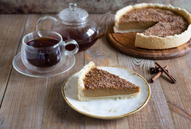 Güzel bir tabakta bir parça balkabağı turtası, ahşap bir tabakta balkabağı turtası ve ahşap bir masada bir fincan sıcak çay..