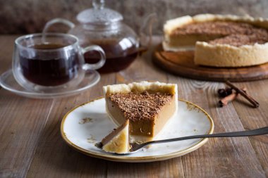 Tabakta bir parça balkabağı turtası, bir bardak çay ve eski ahşap bir masadaki kabak turtası.