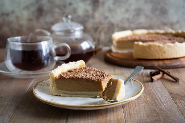 A slice of sweet pumpkin pie with cinnamon on a vintage white plate is photographed close up on a wooden table