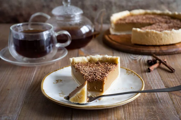 Tabakta bir parça balkabağı turtası, bir bardak çay ve eski ahşap bir masadaki kabak turtası.