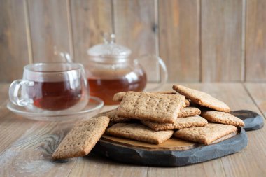 Ön planda lezzetli çikolatalı kurabiyeler, bir fincan çay ve arka planda ahşap bir masada çay olan cam çaydanlık.