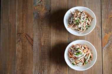 Salatalıklı et salatası ve ahşap bir masada beyaz salata kasesinde baharatlı havuç.