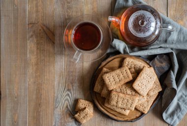 Tahta tabakta krakerler, sıcak çayla demlik, ahşap masada şeffaf bir fincan çay.