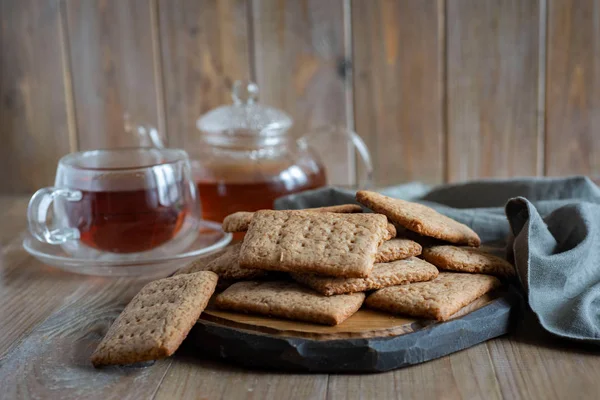 Chocolate crackers on a stylish wooden platter, a glass teapot with hot tea, a beautiful transparent Cup of tea on a wooden table