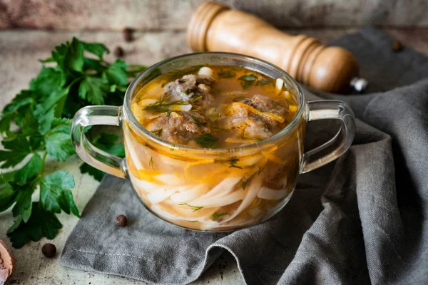 Hot soup with meatballs and noodles in a transparent bowl on a gray background