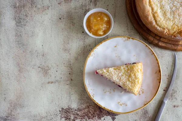 A piece of coconut cake on a white plate, a coconut cake on a wooden plate, and a knife on a gray background