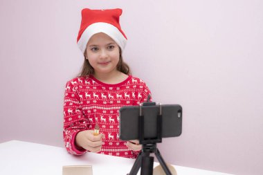 Küçük sevimli blogcu kız takipçileri için akıllı telefondan video kaydediyor. Telefon kamerasına bakmak, masadaki kozmetik ürünler, video yayını. Sevimli çocuk yeni teknoloji öğreniyor. Akıllı telefonu olan küçük bir kız..