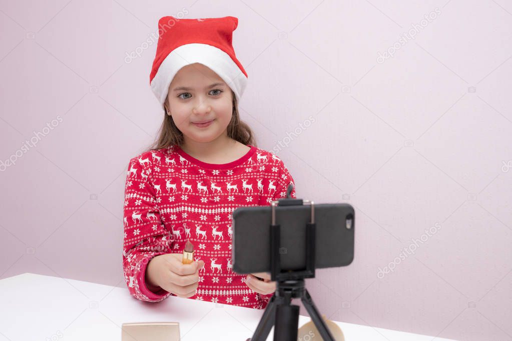 beautiful cute little blogger girl recording a video on smartphone for her followers. looking at the phone camera, cosmetics on the table, Video streaming. Adorable child learning new technology. Small girl child with smartphone.