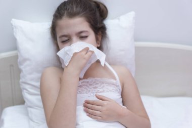 Küçük kız yatağında oturmuş mendile hapşırıyor..