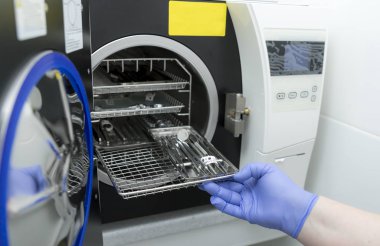 Tıbbi ekipmanları sterilize etmek için bir makine. Otoklavda tıbbi aletler sterilize ediliyor. Diş hekimliği. Dişçi asistanının elleri otoklavın tıbbi aletlerini sterilize ediyor. Seçici odaklanma. Steril diş aletleri