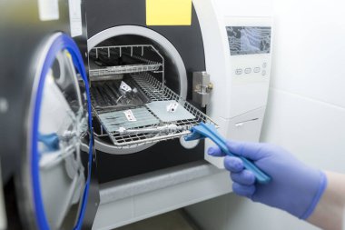 Tıbbi ekipmanları sterilize etmek için bir makine. Otoklavda tıbbi aletler sterilize ediliyor. Diş hekimliği. Dişçi asistanının elleri otoklavın tıbbi aletlerini sterilize ediyor. Seçici odaklanma. Steril diş aletleri