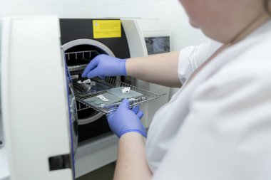 Tıbbi ekipmanları sterilize etmek için bir makine. Otoklavda tıbbi aletler sterilize ediliyor. Diş hekimliği. Dişçi asistanının elleri otoklavın tıbbi aletlerini sterilize ediyor. Seçici odaklanma. Steril diş aletleri