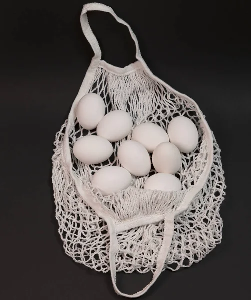 freshe white eggs with in white string shopping bag on black background with copy space. Zero waste shopping concept