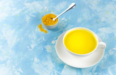 Mavi arka planda bir bardakta zerdeçal içeren altın süt. Sağlıklı doğal enerji içeceği. Moda detoks, bağışıklık güçlendirici, iltihap önleyici sağlıklı içecek. Altın latte, zerdeçal sütü, detoks, bağışıklık güçlendirici, iltihap önleyici sağlıklı içecek.