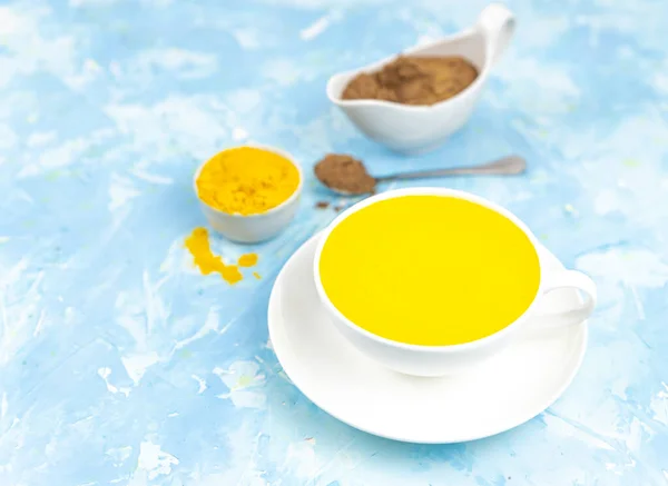 Golden milk with turmeric in a glass on a blue background. healthy natural energy drink.Trendy detox, immune boosting, anti-inflammatory healthy cozy drink. golden latte, turmeric milk, Detox, immune boosting, anti inflammatory healthy cozy drink