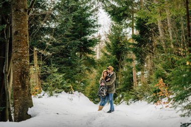 Karlı bir günde kozalaklı ormanda sevişen bir çift. Kış tatili